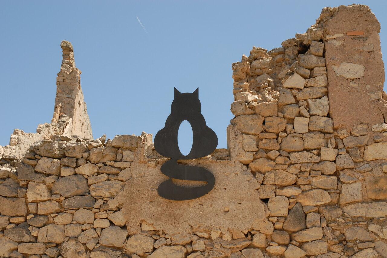 Black letter G artwork from the Abecedari de la Llibertat mounted among ruined stone walls