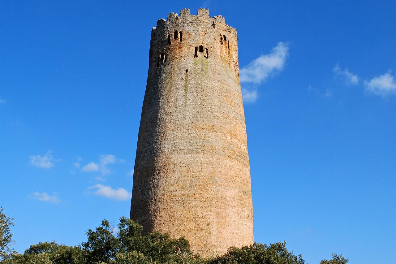 The tall round masonry shaft and crenellated crown of Vallferosa Tower seen from below